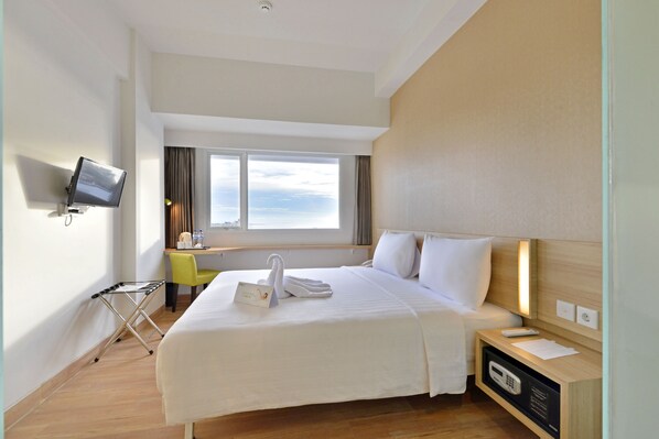 Habitación de hotel con cama, escritorio, televisor y ventana con vista al cielo.