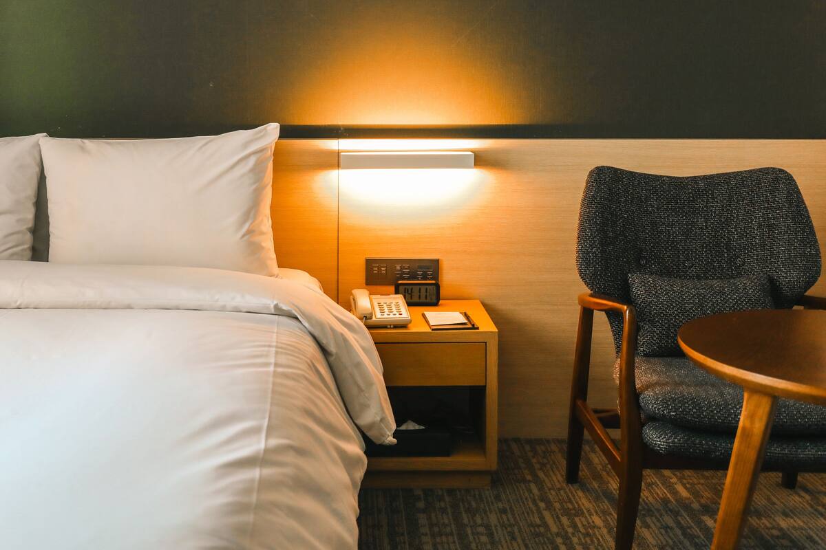Une chambre d’hôtel avec un lit, une table de chevet avec un téléphone et une horloge, une chaise et une petite table.