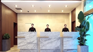 A reception desk with marble tops, wooden paneling, and a large potted plant.