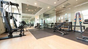 A gym with various exercise equipment, a mirror wall, and a wooden floor.
