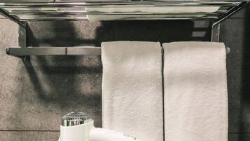Ein Badezimmer mit Duschkabine aus Glas, einem Handtuchhalter mit gefalteten Handtüchern und einem Haartrockner auf dem Boden.