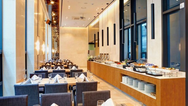 A modern dining area with long tables, chairs, and a buffet counter with various food items.