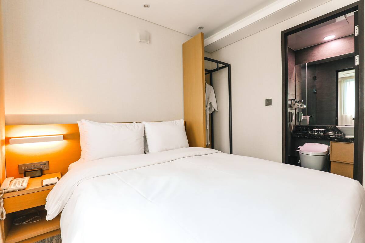 Une chambre d’hôtel avec un lit, une lampe de chevet, un téléphone et un miroir.