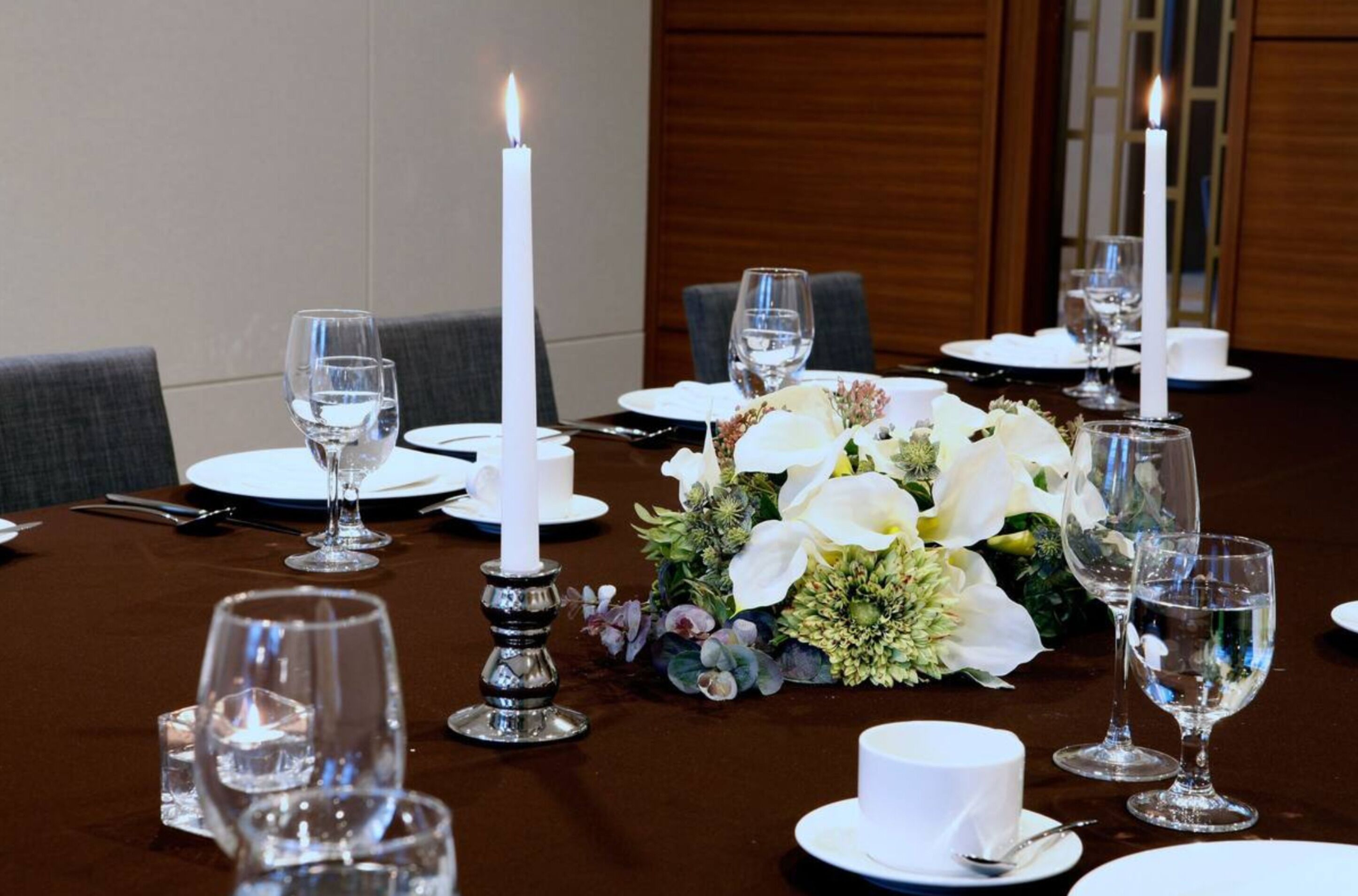 A dining table set with white plates, glasses, and a centerpiece of white flowers.