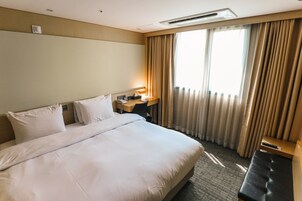 Un cuarto de hotel con una cama grande, un escritorio con lámpara y vistas al exterior a través de la ventana.