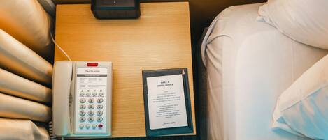 Habitación de hotel con teléfono en la mesita de noche, un dispositivo SnoozeLight y una tarjeta de información sobre opciones ecológicas.