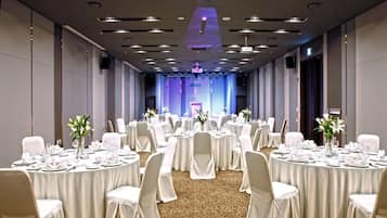 Un salón de banquetes con mesas redondas, sillas blancas y centros de mesa florales.