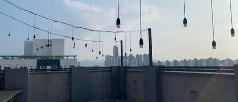 Una terraza en la azotea con piso a cuadros, luces colgantes y el horizonte de la ciudad al fondo.