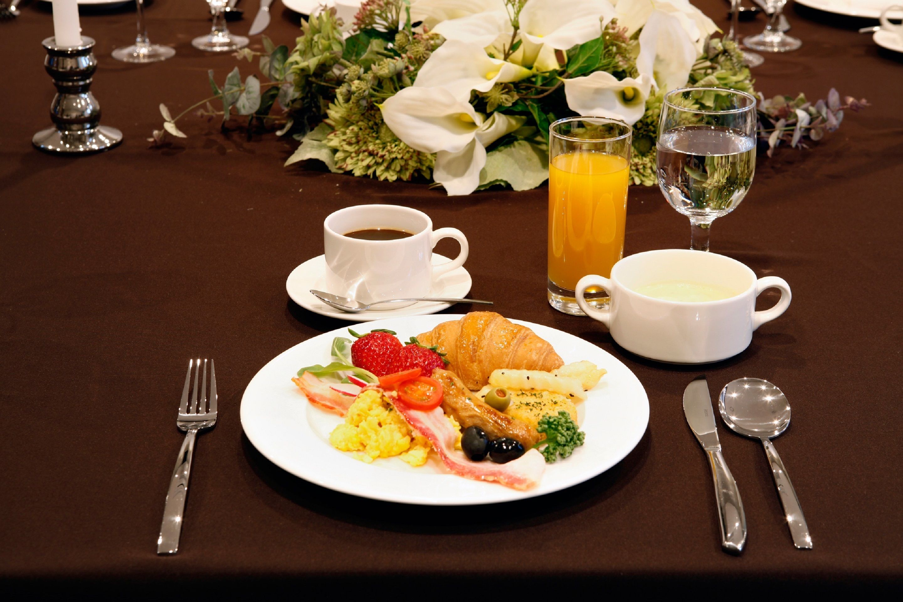 A breakfast table with a croissant, scrambled eggs, bacon, strawberries, and a glass of orange juice.