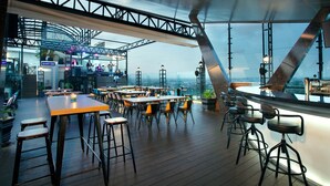 Een eethoek met tafels en stoelen, een podium voor live muziek, en een uitzicht op de stad door grote ramen.