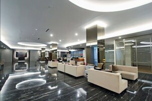 A modern lobby with a marble floor, seating areas, and a reception desk.
