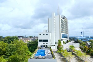 Un hotel moderno con piscina, rodeado de exuberante vegetación y un cielo despejado.