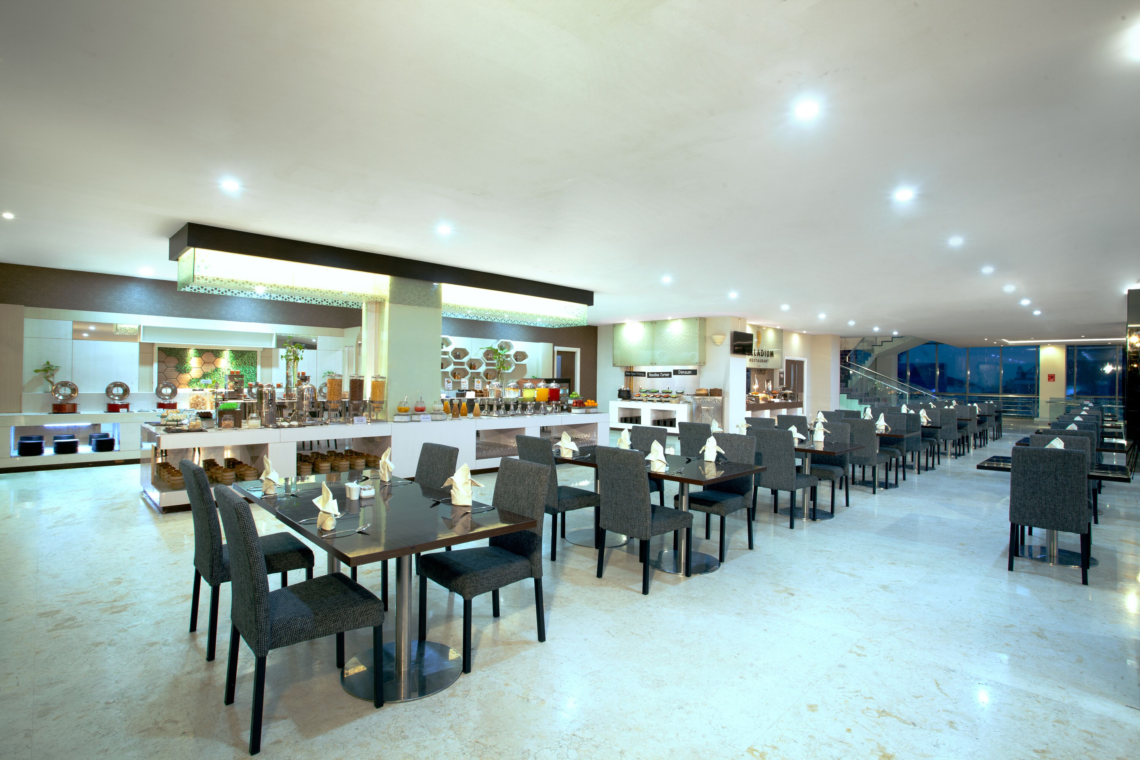 A spacious hotel lobby with a central bar area, multiple seating arrangements, and a staircase leading to upper floors.
