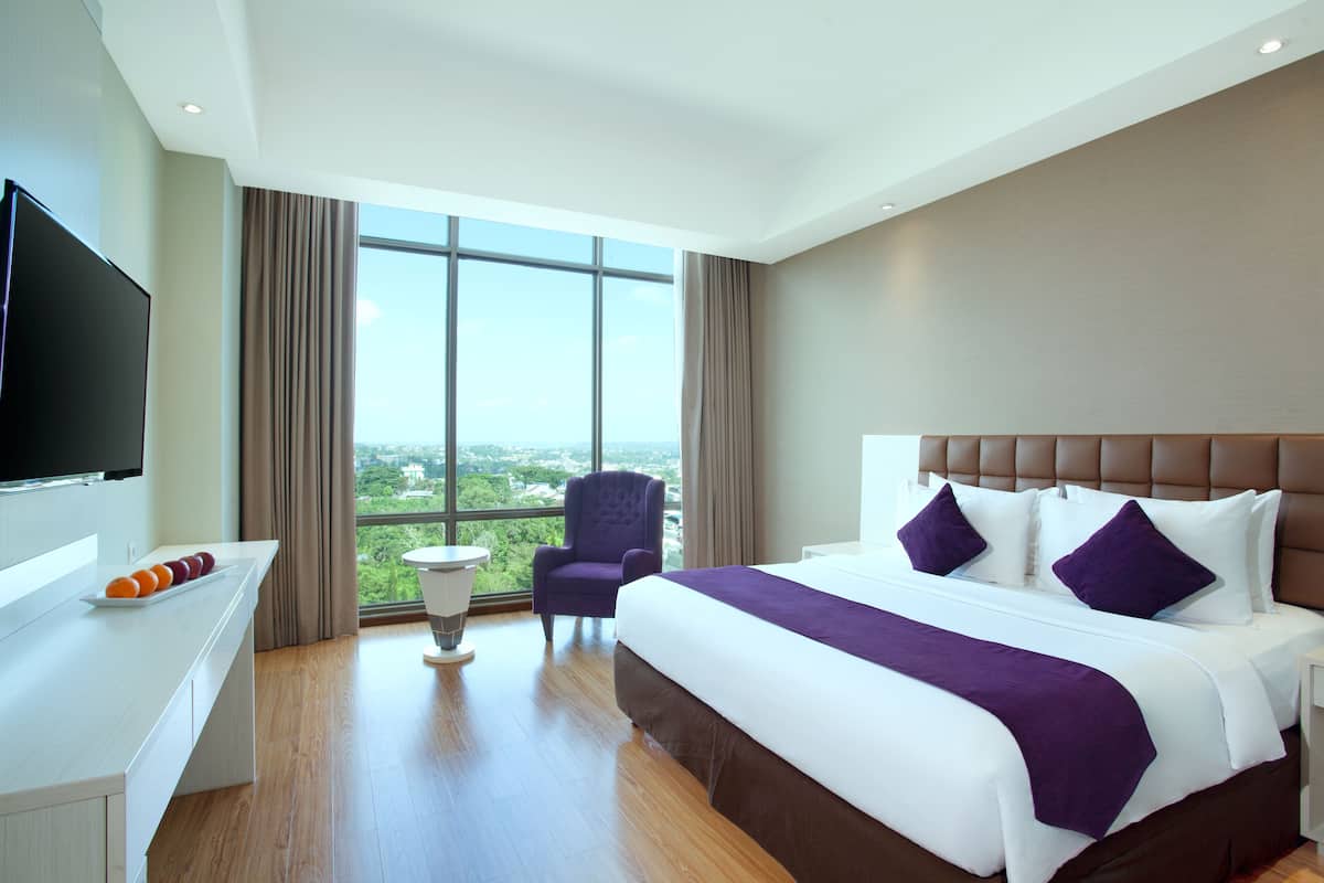 Una habitación de hotel con una cama grande, televisor, una mesita y una silla.