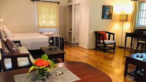 Una habitación de hotel acogedora con una cama, una mesita con un florero, una silla y un escritorio con una lámpara.
