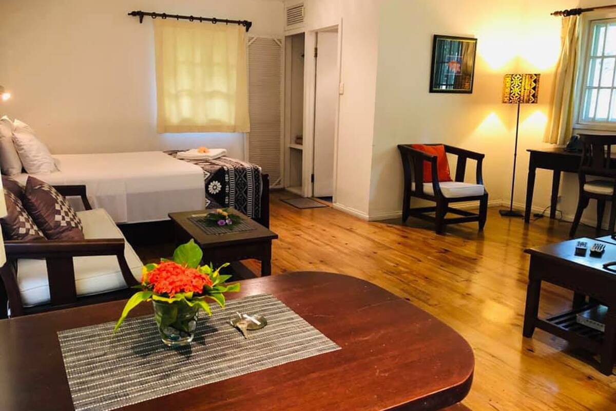 A cozy hotel room with a bed, a small table with a vase of flowers, a chair, and a desk with a lamp.