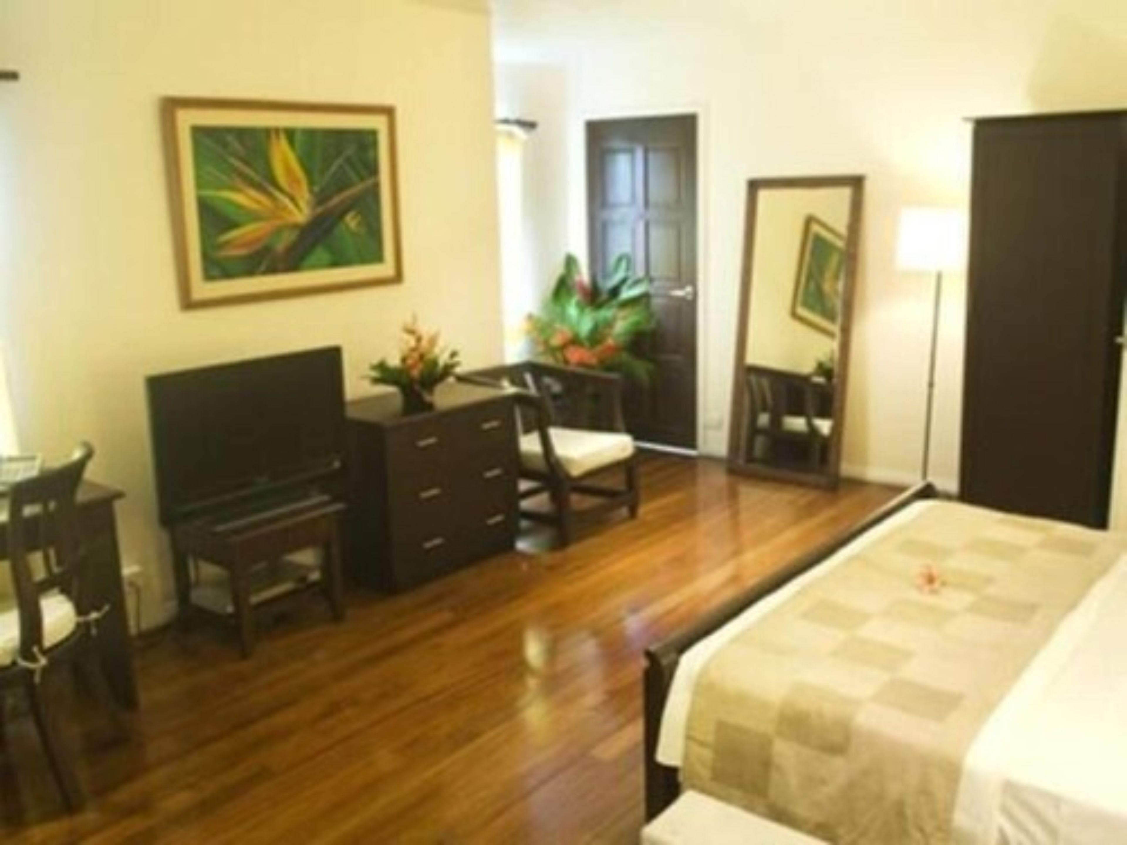 A hotel room with a bed, a desk with a chair, a television, a dresser, and a mirror.
