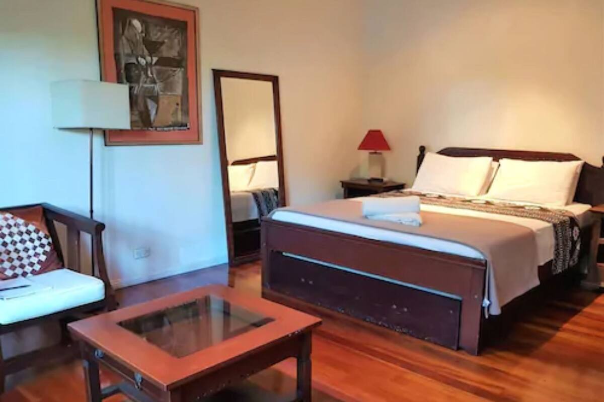 A hotel room with a wooden bed, a bedside table, a chair, and a desk with a glass top.