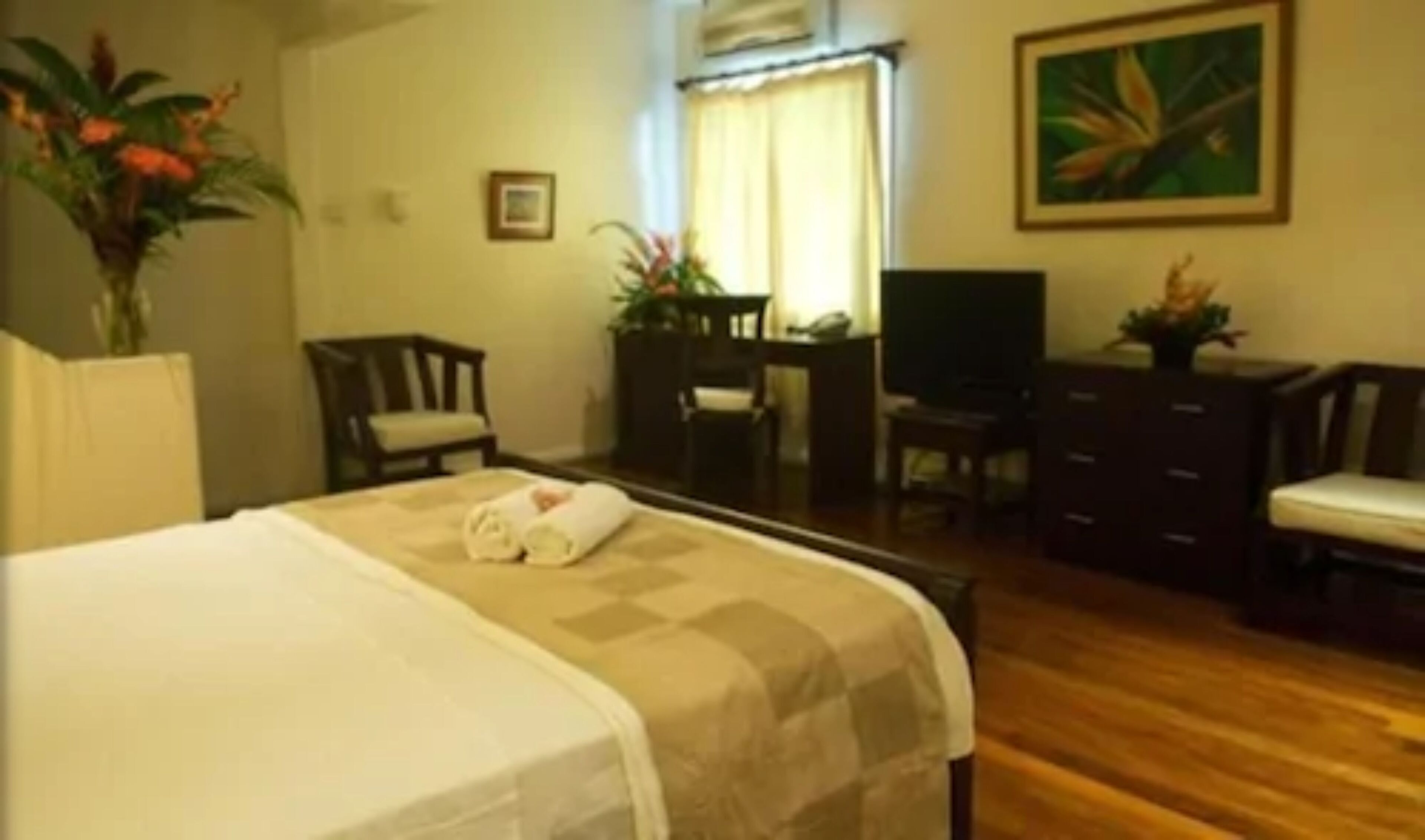 A hotel room with a bed, a desk, a chair, a television, and a painting on the wall.