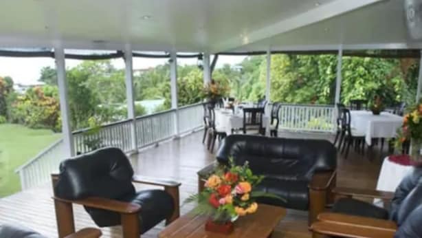Un patio techado al aire libre con mobiliario de madera, incluyendo sofás y una mesa de centro con un centro de mesa floral.