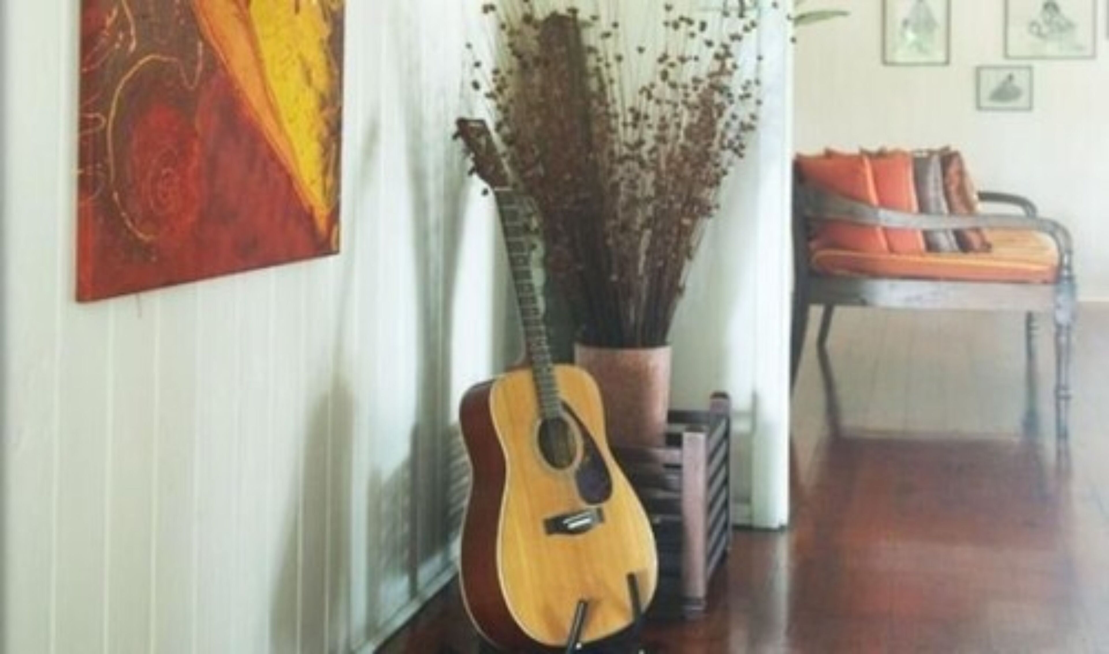 A room with a guitar, a potted plant, and a chair with cushions.