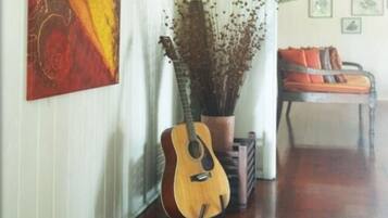 A room with a guitar, a potted plant, and a chair with cushions.