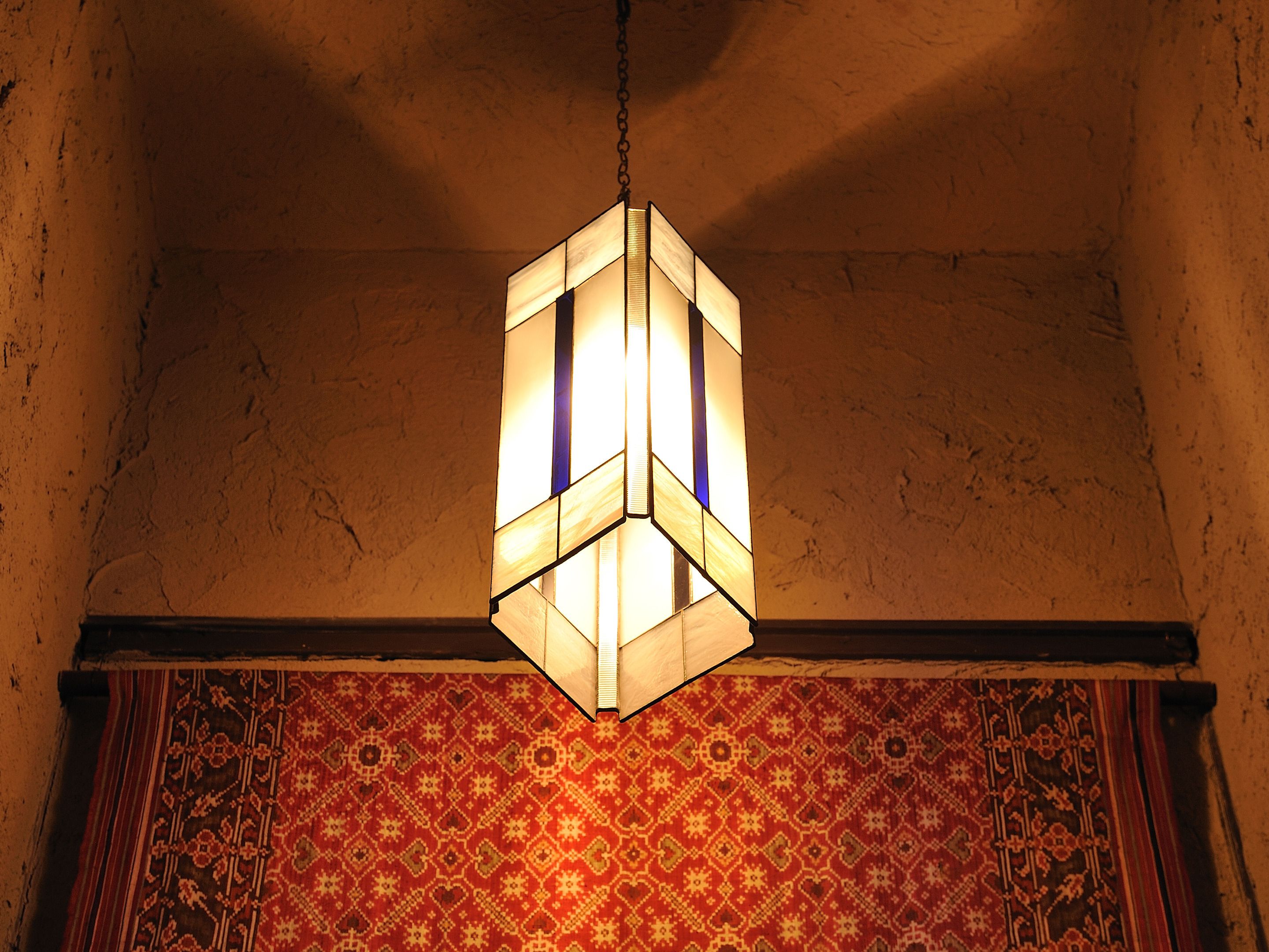 A geometric hanging light fixture in a room with patterned wall hanging.