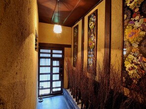 A hallway with a wooden ceiling, a hanging light fixture, a door with a grid pattern, and a wall with floral designs. - Theatre and Library Residence -Kyoto Imagumano- (Kyoto)