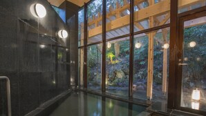 Un área de spa con cerramiento de vidrio, vigas de madera y vista a un paisaje boscoso.