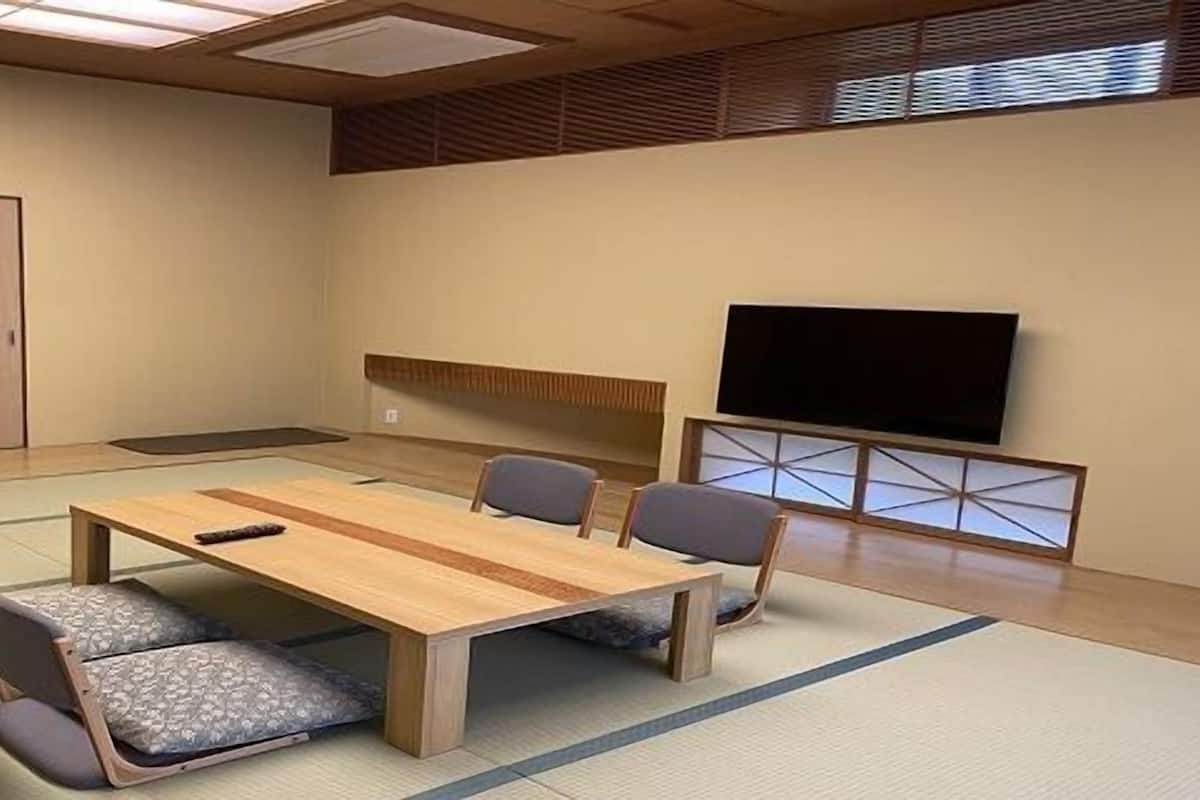 A conference room with a wooden table, four chairs, tatami mats, a television, and a sliding door.