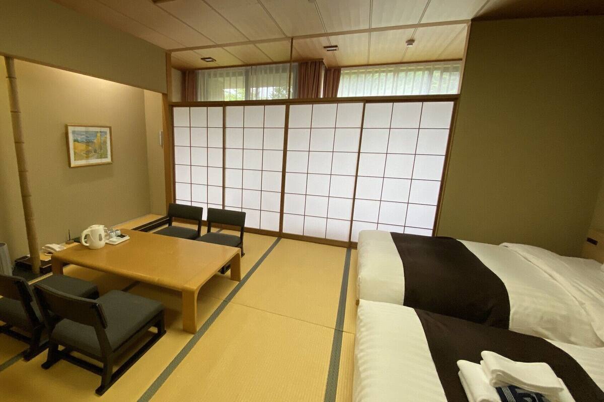 Habitació d'hotel amb paviment de tatami, una taula baixa amb cadires, un llit, una televisió i un panell shoji.