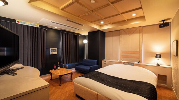 A hotel room with a bed, a desk with a computer, a chair, a TV, and a minibar. - Hotel Saint Martin – Adults Only (Kyoto)