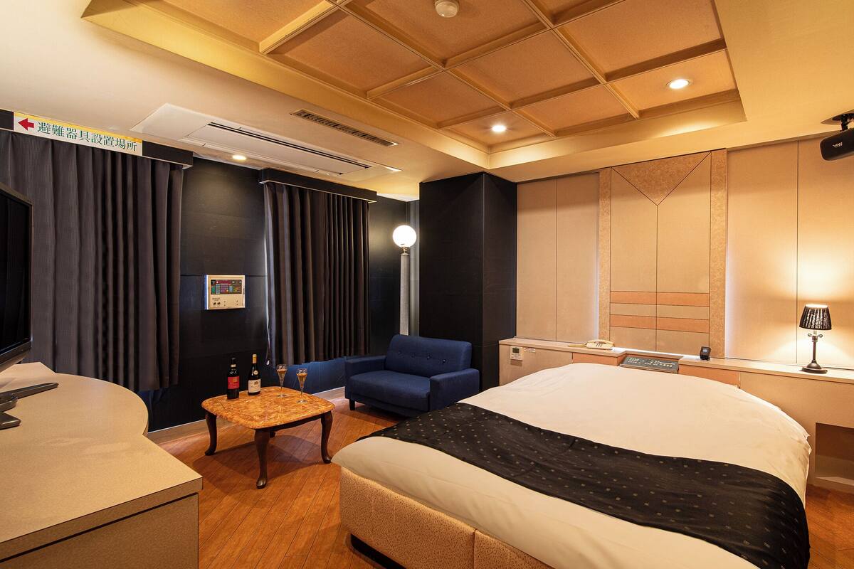 A hotel room with a bed, a desk with a computer, a chair, a TV, and a minibar.