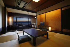 A modern room with tatami flooring, a dark wooden table, and a TV on the wall. - Hotel Nampuro (Shimabara)