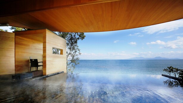 An infinity pool with a clear view of the sea and mountains, wooden deck, and a modern building structure. - Hotel Nampuro (Shimabara)