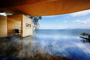 Une piscine à débordement offrant une vue imprenable sur la mer et les montagnes, une terrasse en bois et une structure de bâtiment moderne.