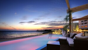 A poolside area with a view of the ocean at sunset, wooden deck, and outdoor seating. - Hotel Nampuro (Shimabara)