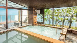 A spa area with a hot tub, wooden deck, and a view of the water. - Hotel Nampuro (Shimabara)