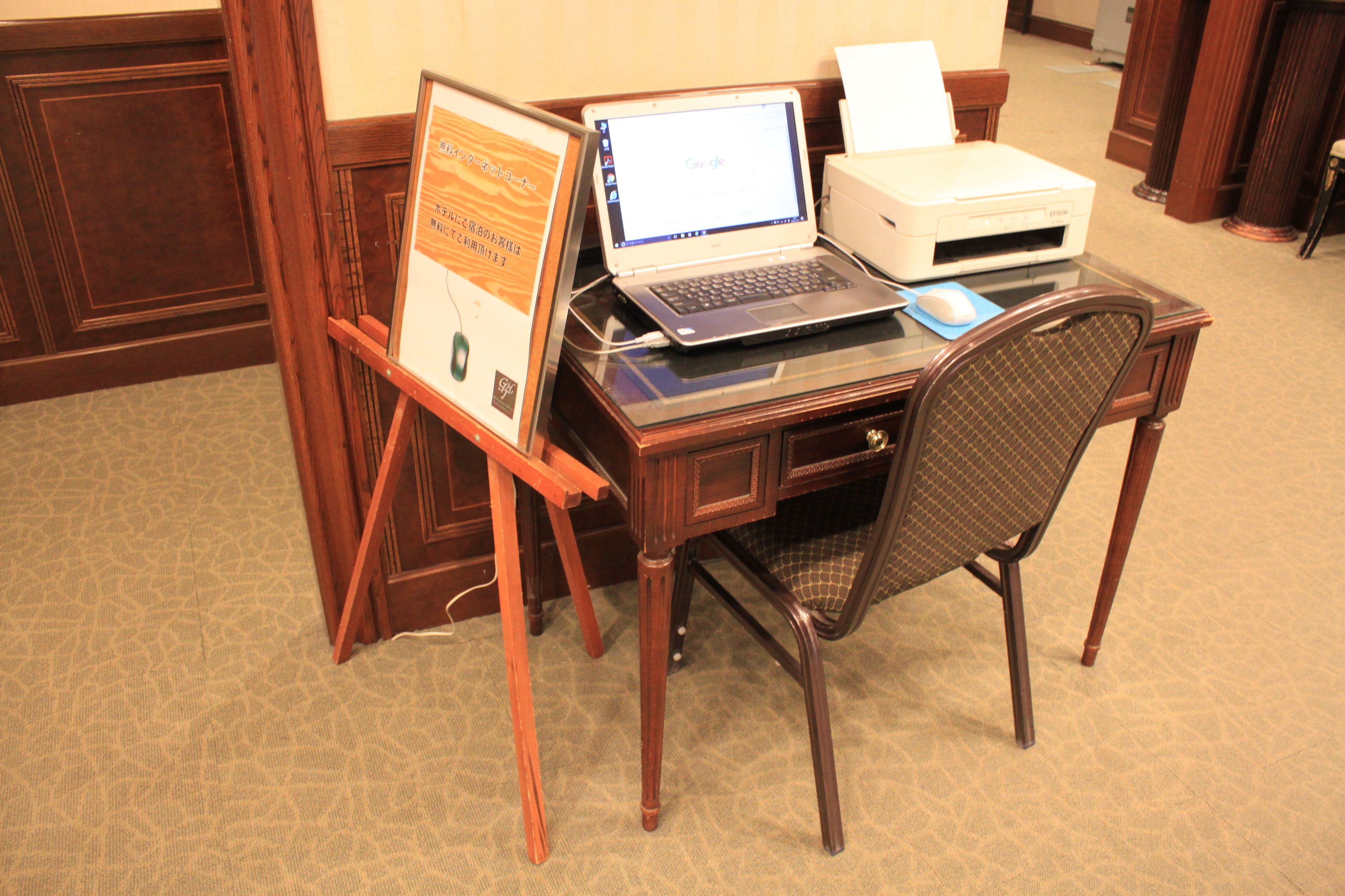 Un bureau en bois avec un ordinateur portable, une imprimante et un document encadré.
