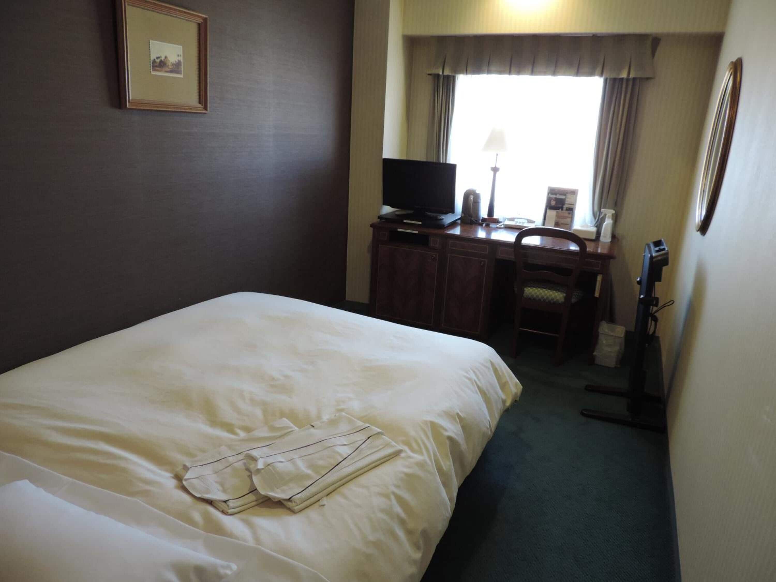 A hotel room with a large bed, a desk with a computer, a chair, and a television.