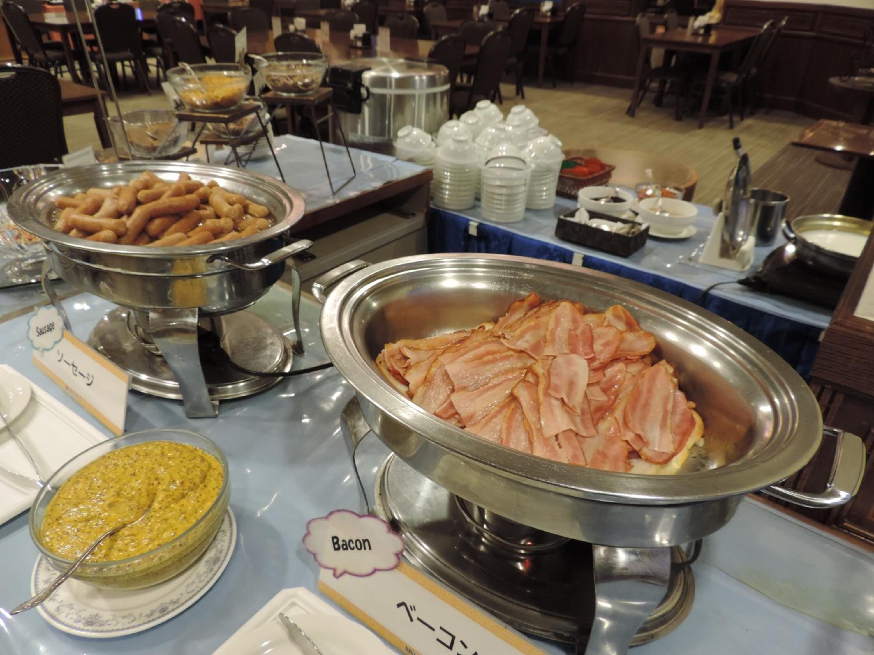 A buffet with various food items including sausages, bacon, and a bowl of soup.