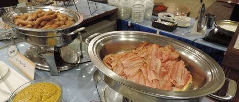 A buffet with various food items including sausages, bacon, and a bowl of soup.