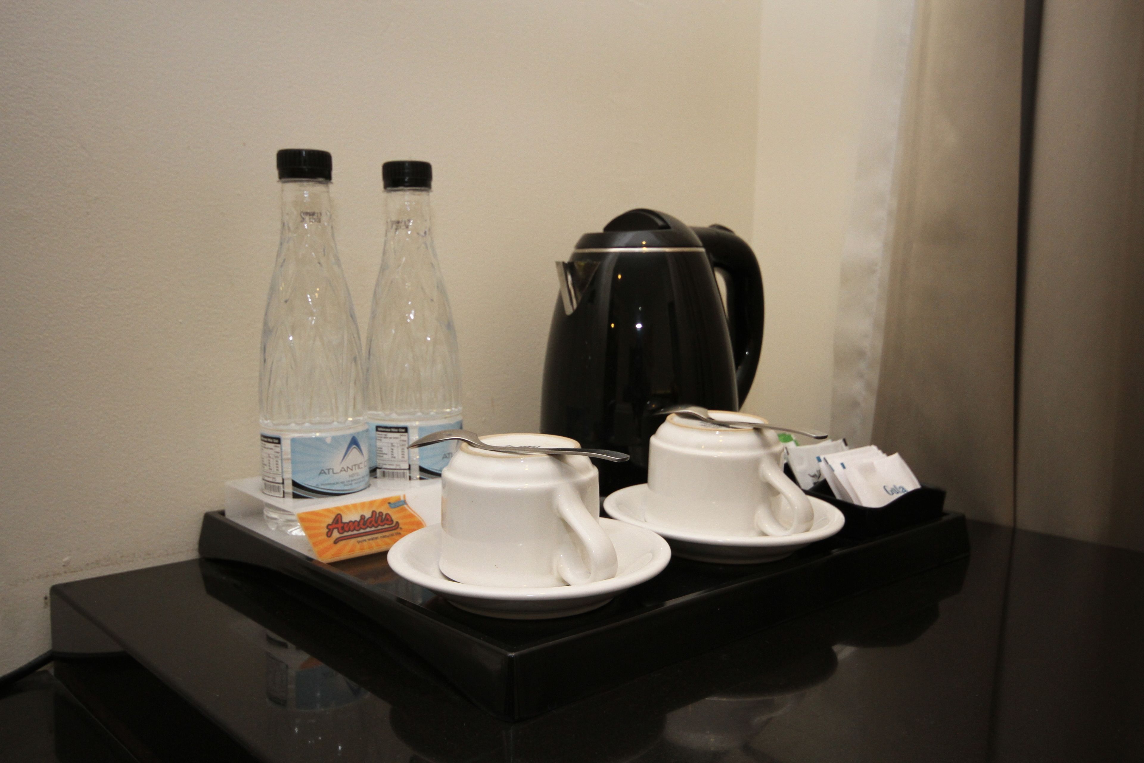 Frühstücksaufstellung in einem Hotelzimmer mit zwei Glasflaschen, einer schwarzen Kaffeemaschine und zwei weißen Tassen auf einem Tablett.