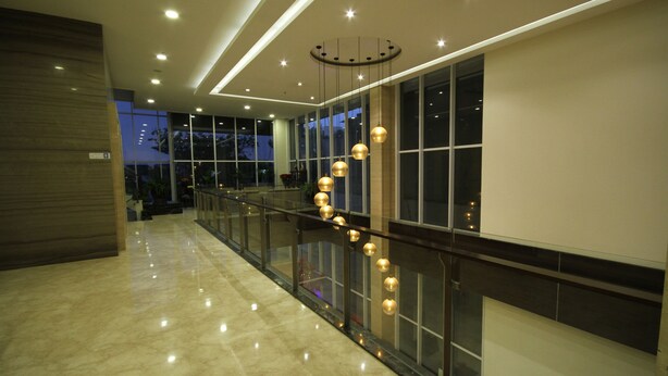 Corredor moderno de hotel com guarda-corpo de vidro, diversos luminários esféricos pendentes e piso de mármore polido.