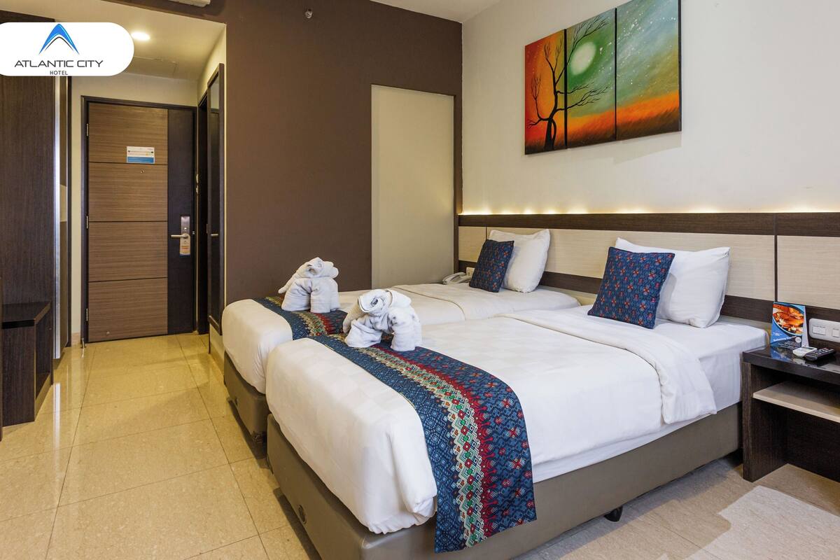 A hotel room with two beds, a nightstand, a painting, and a door.