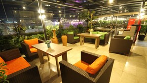 Um lounge no terraço com móveis de vime, uma mesa e plantas em vasos.