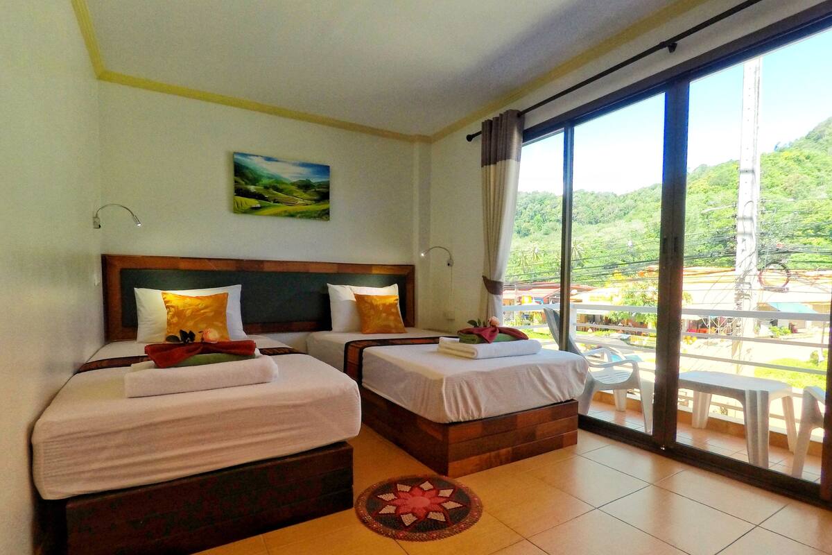 A hotel room with two beds, a view of the outdoors, and a balcony with chairs.
