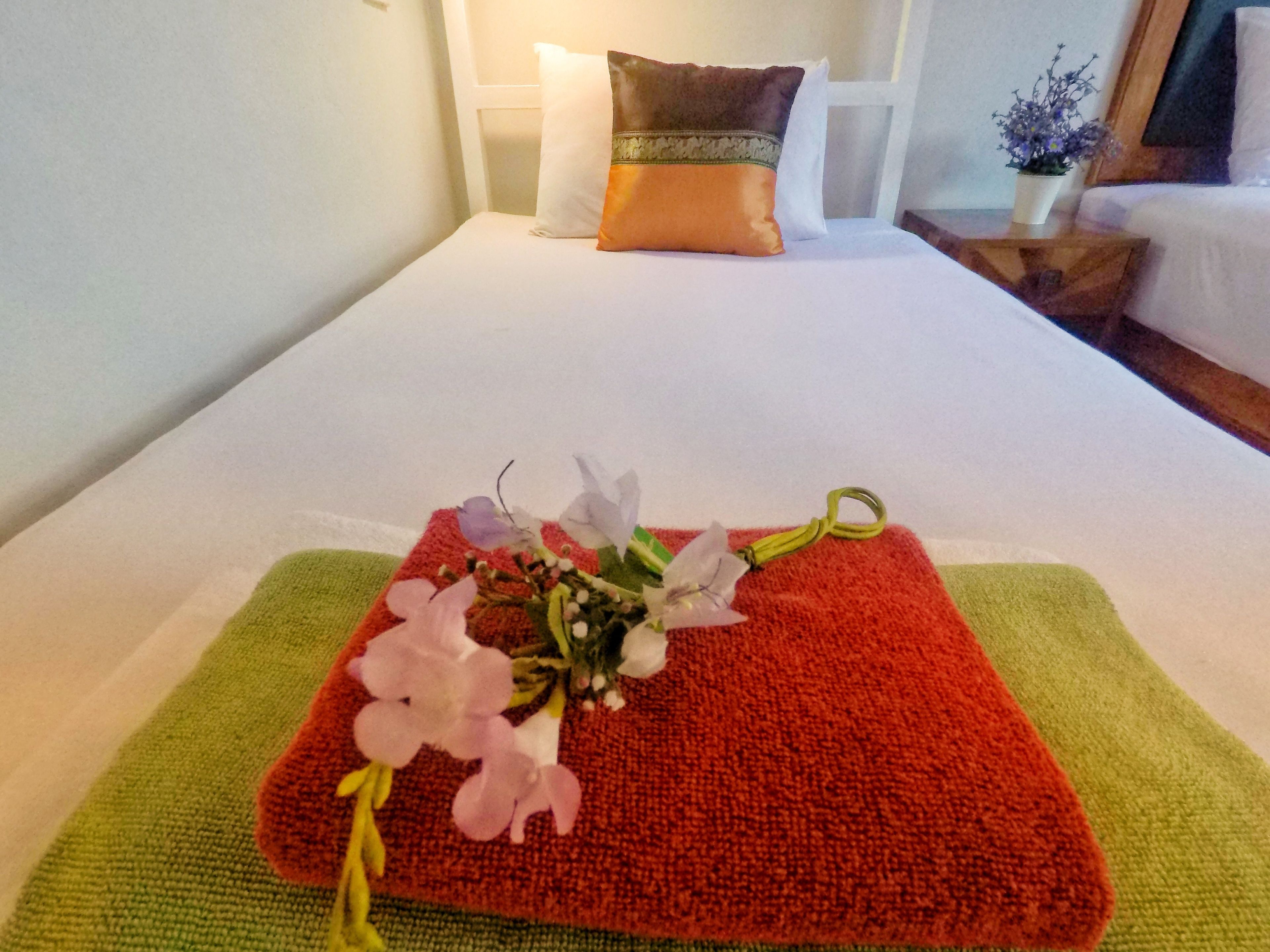A neatly made bed with a red and green towel, a white pillow, and a small potted plant on the nightstand.