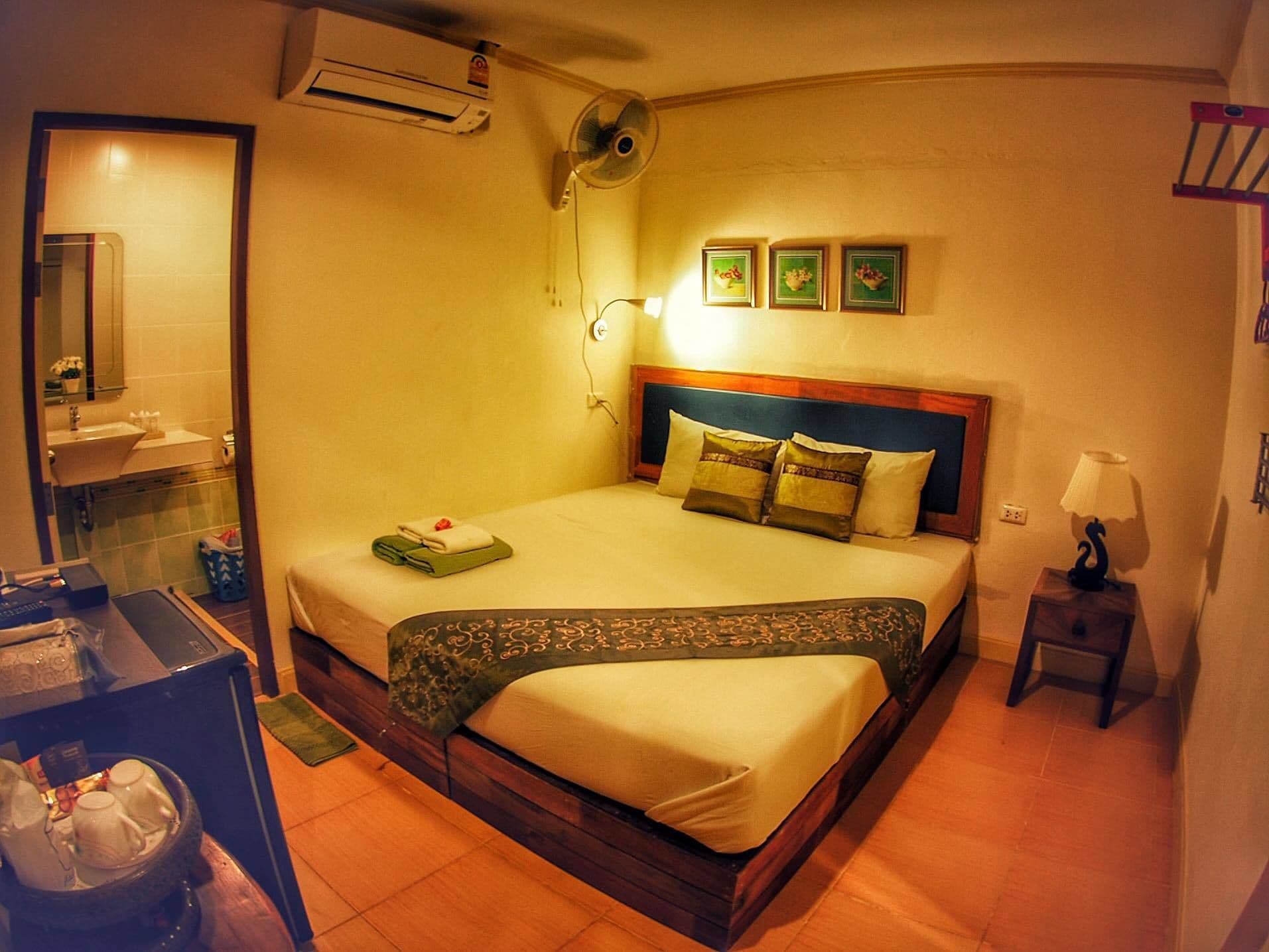 Habitación de hotel con cama, mesita de noche con lámpara, una pequeña mesa con jarra de agua y espejo sobre el lavabo.