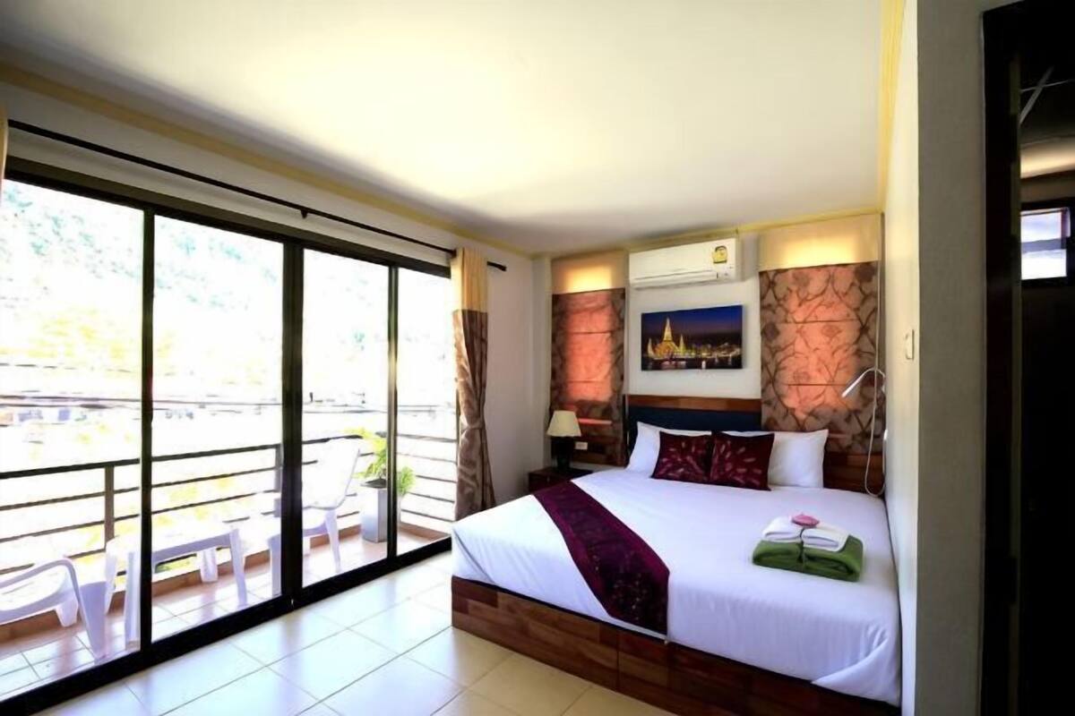 Habitación de hotel con una cama grande, un balcón con sillas y vistas a la ciudad.